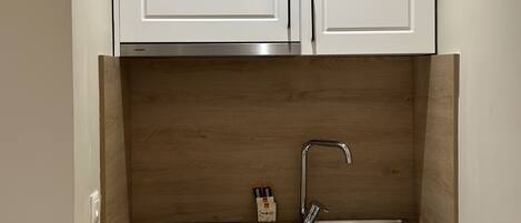 Cocina compacta con armarios blancos, un lavamanos de acero inoxidable y un protector de pared de madera.