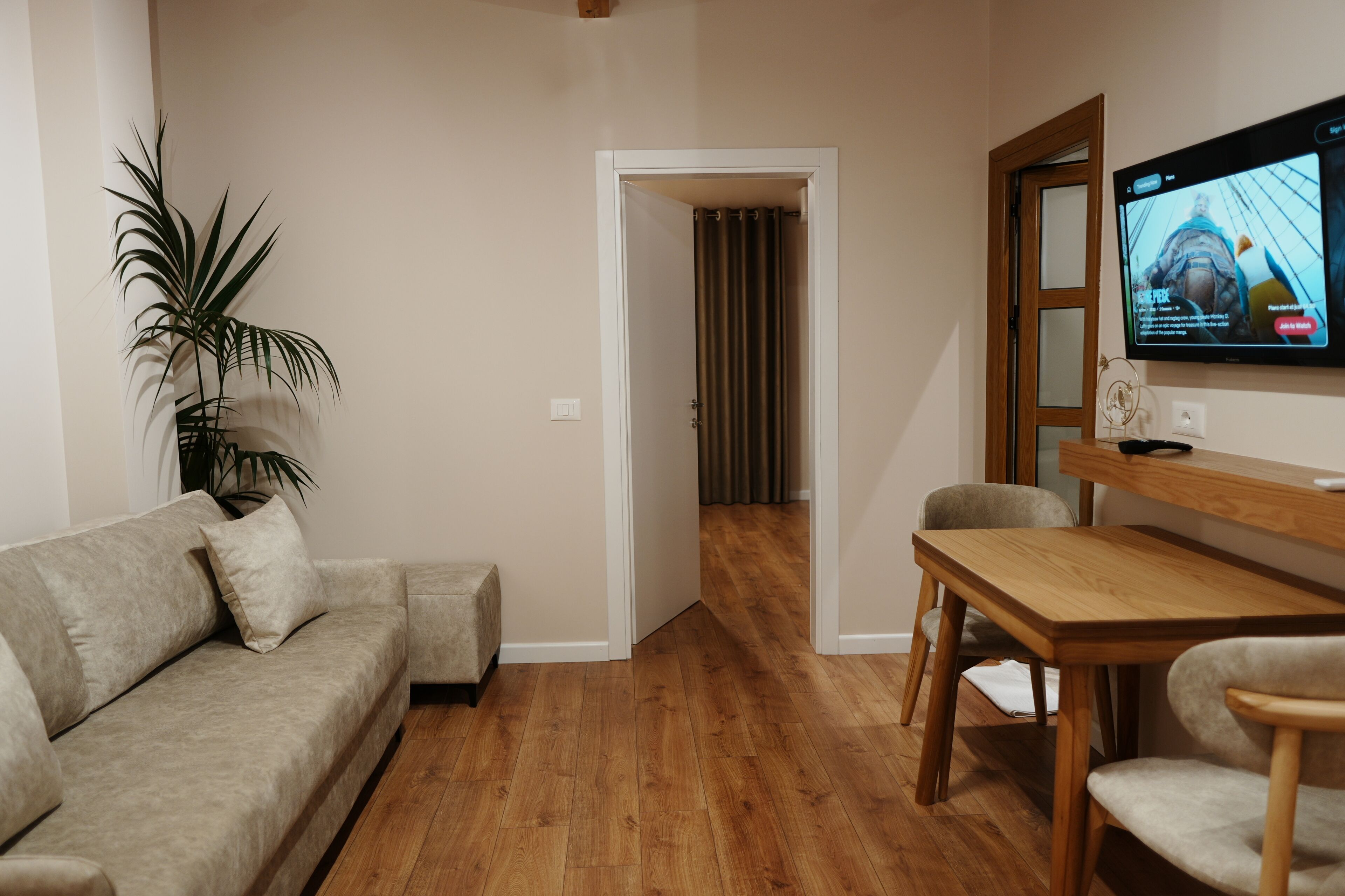 A living room with a sofa, a dining table, a TV, and a plant.