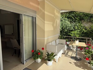 A balcony with a white wicker sofa, a small table, and potted plants.