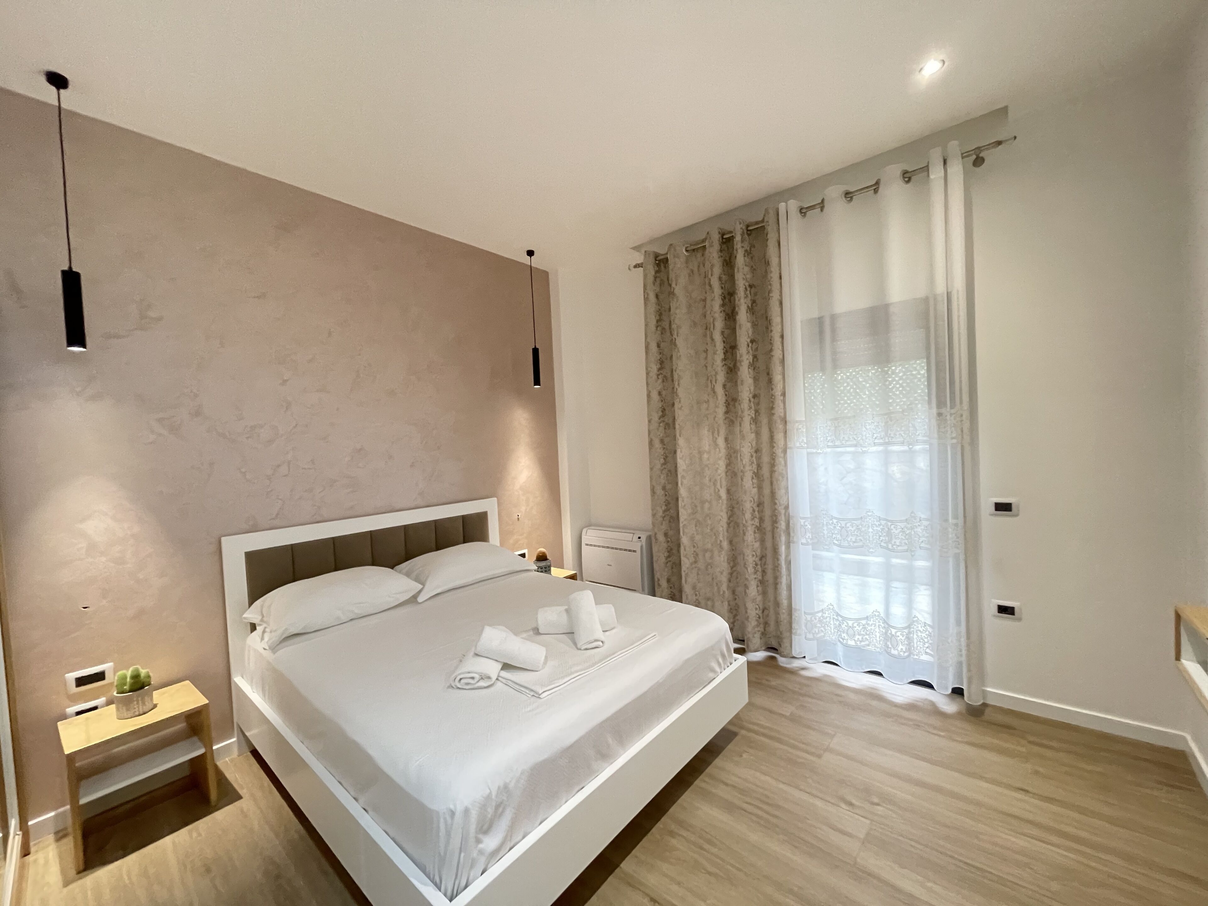 A modern bedroom with a large bed, bedside tables, a nightstand, and a window with curtains.