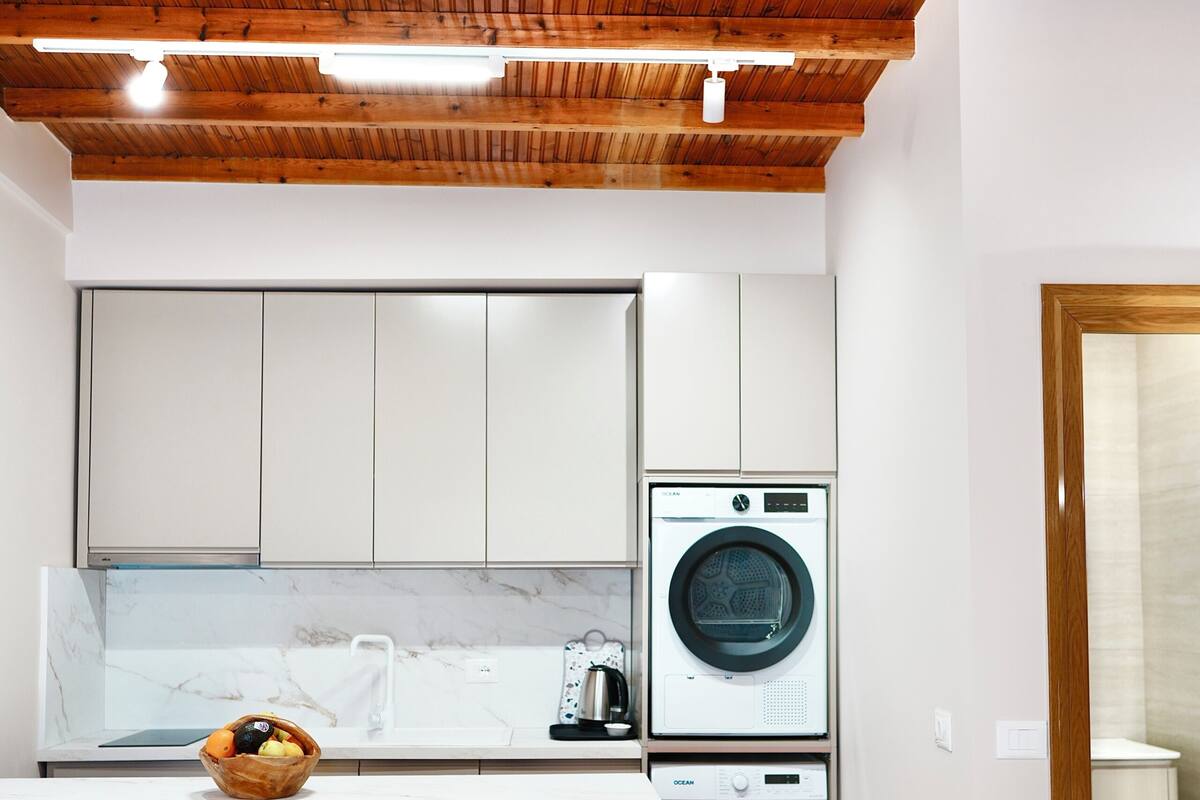 A compact kitchen with wooden ceiling beams, a washing machine, and a seating area with stools.