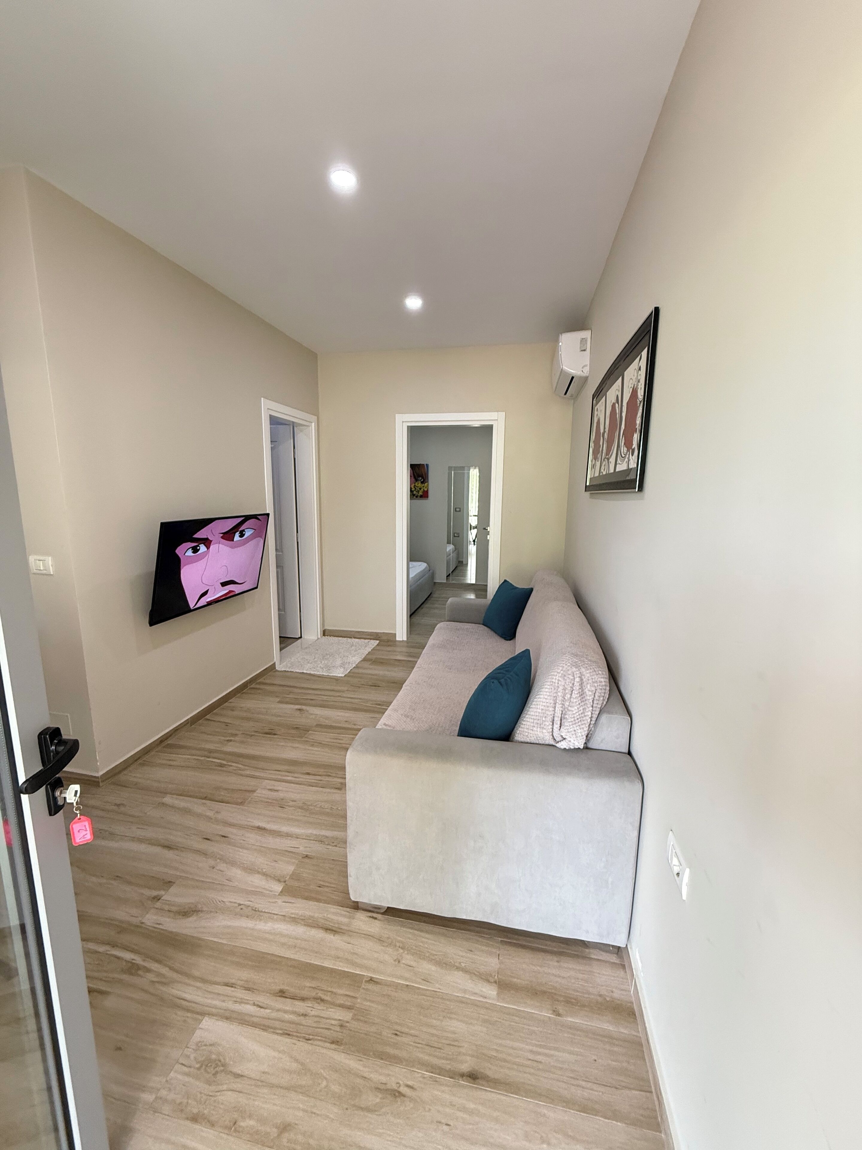 A modern living room with a beige sofa, a flat-screen TV, and a wooden floor.