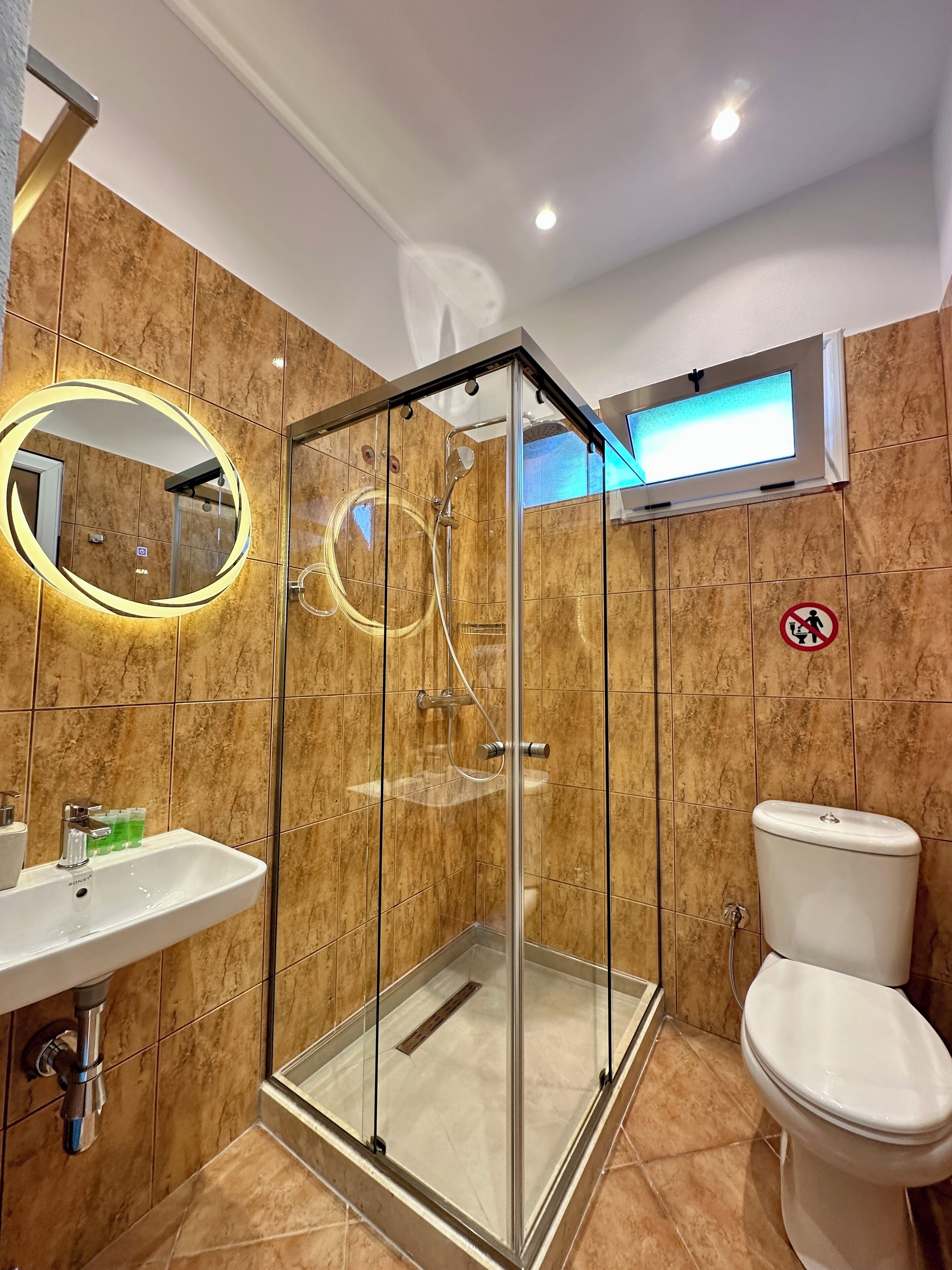 A modern bathroom with a glass-enclosed shower, a sink with toiletries, and a toilet.