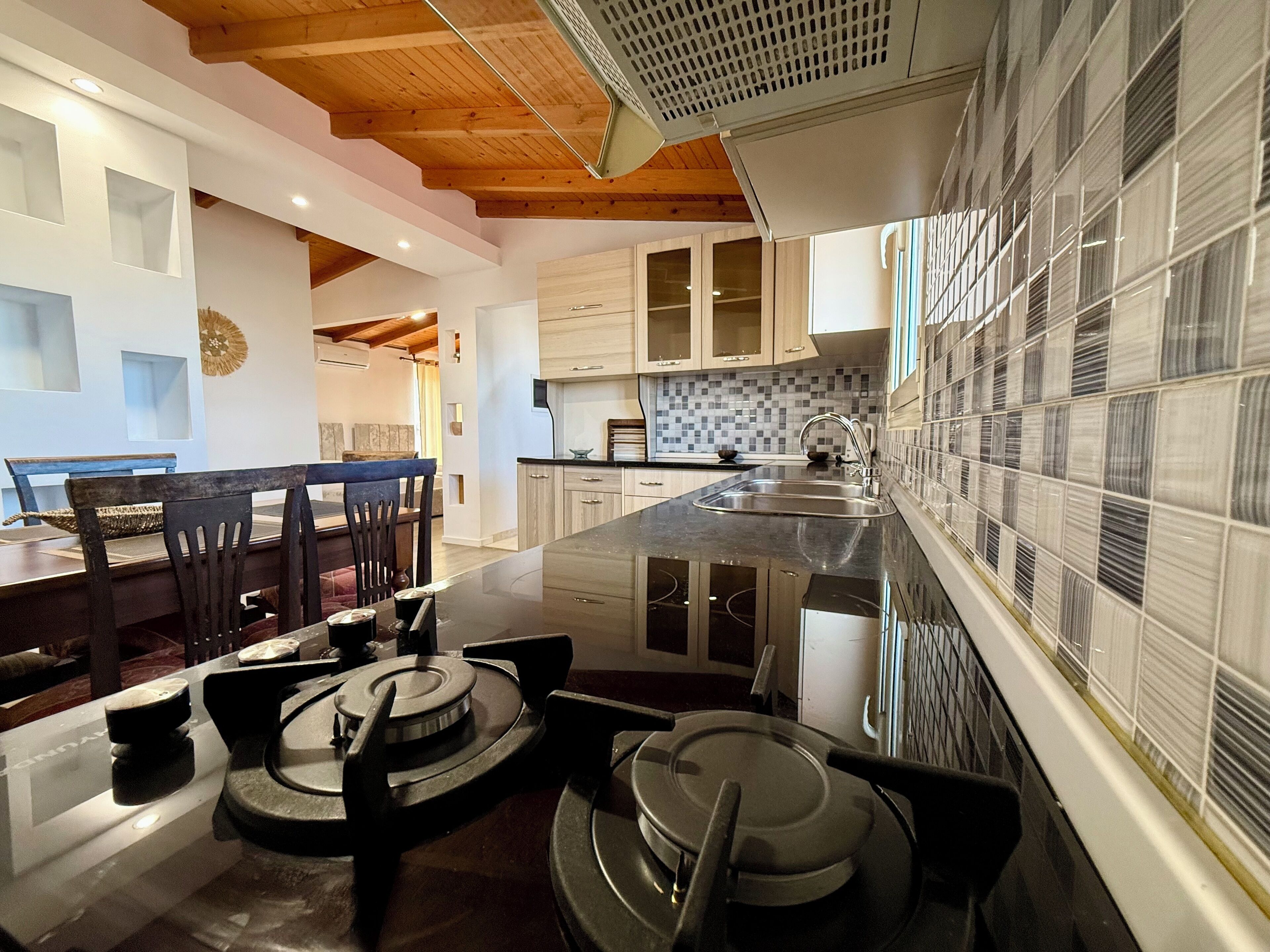 Una cucina moderna con isola centrale, travi in legno al soffitto e paraschizzi piastrellato.