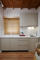 Una cocina con vigas de madera, un lavamanos, armarios y una ventana con persianas.
