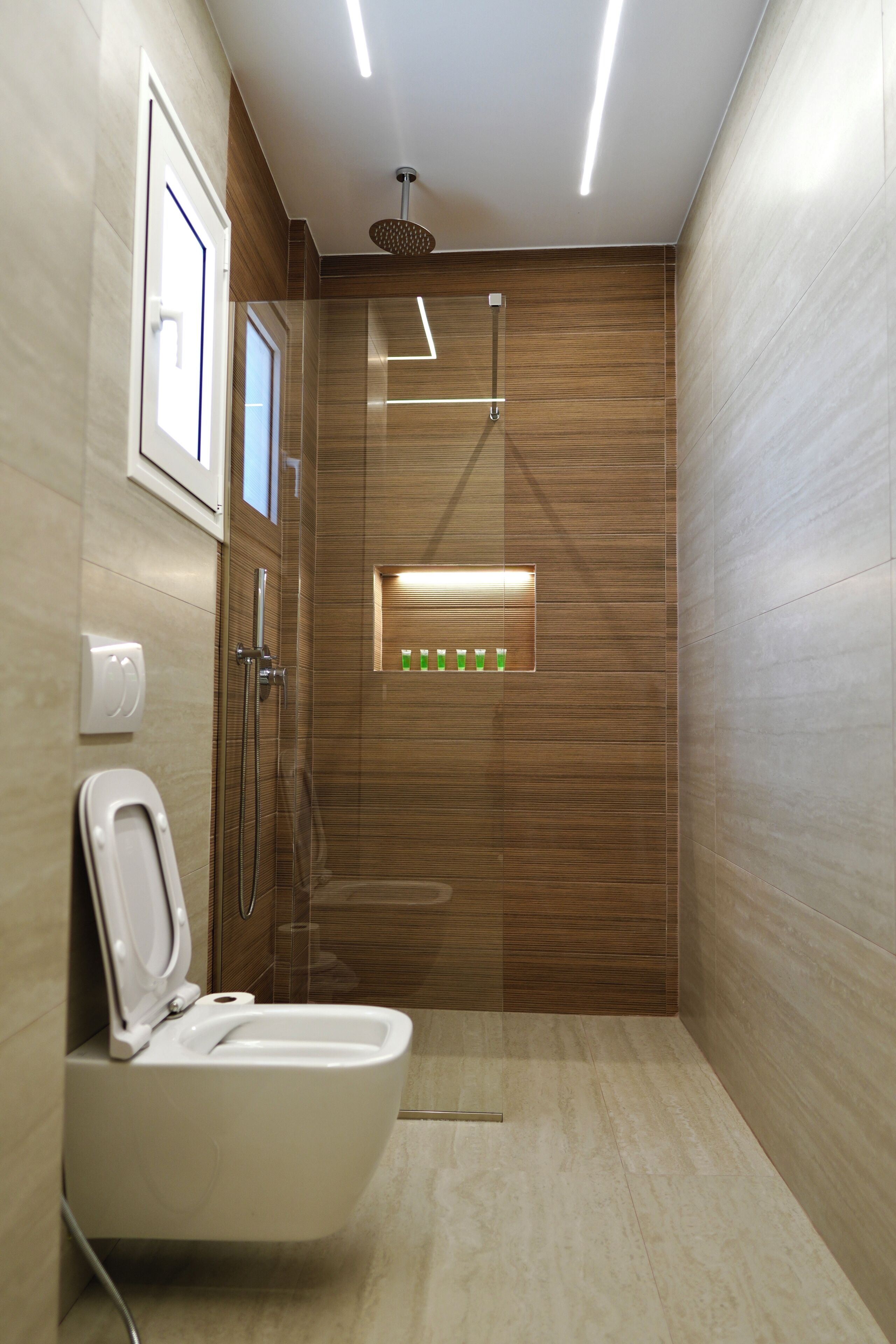 A modern bathroom with a toilet, shower, and a small window with green bottles.