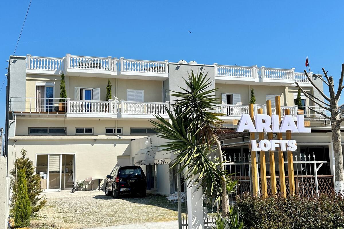 A multi-story building with balconies, a sign for 'ARIAL LOFTS', and a parked car in front.