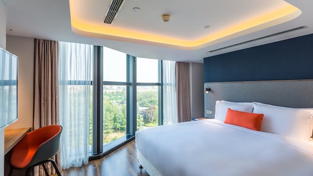 Habitación de hotel moderna con una cama grande, un escritorio y vistas a zonas verdes a través de amplios ventanales.