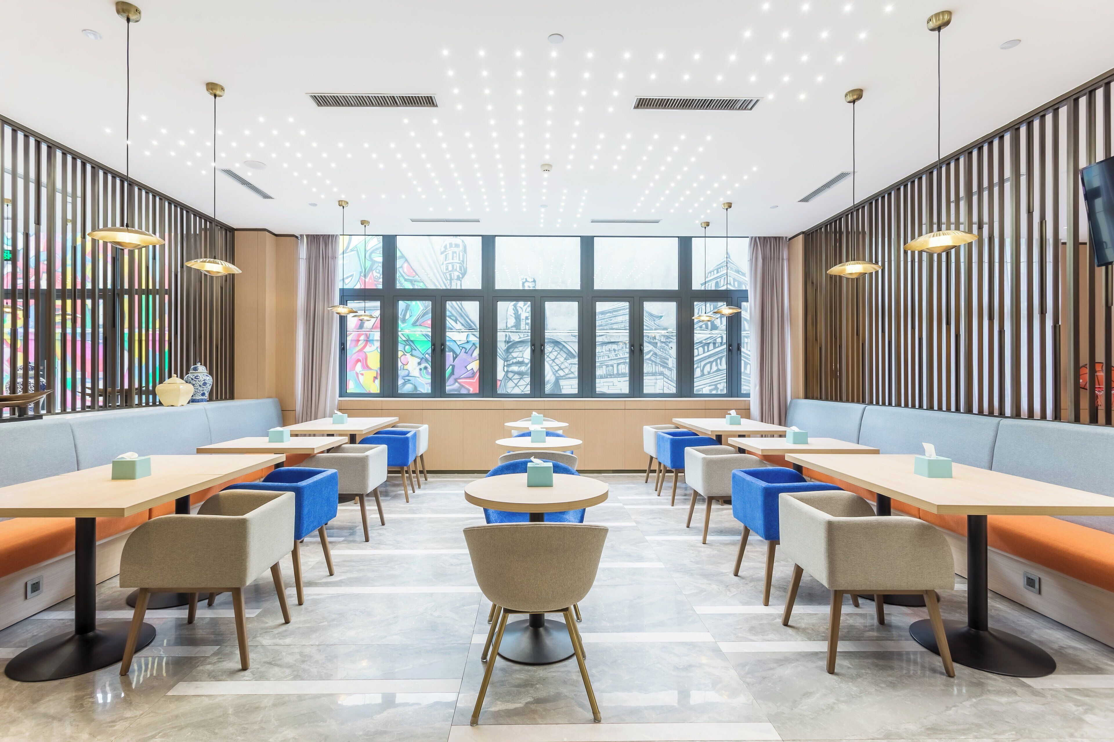 A modern dining area with booths and tables, large windows, and a ceiling with recessed lighting.