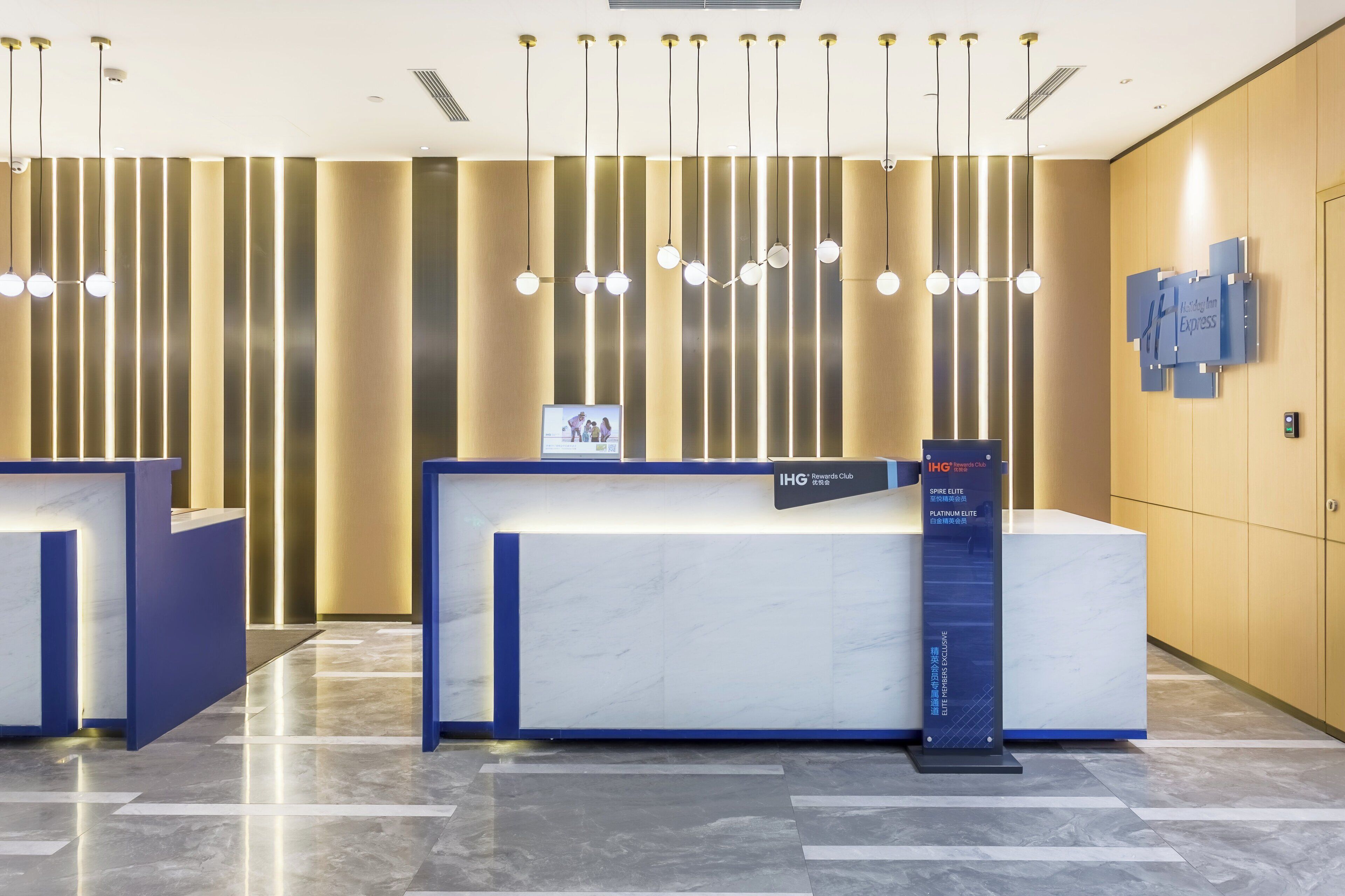 A hotel reception area with a marble reception desk, vertical light fixtures, and a sign for the Holiday Inn Express.