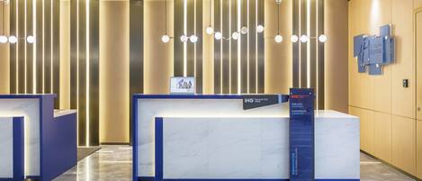 A hotel reception area with a marble reception desk, vertical light fixtures, and a sign for the Holiday Inn Express.