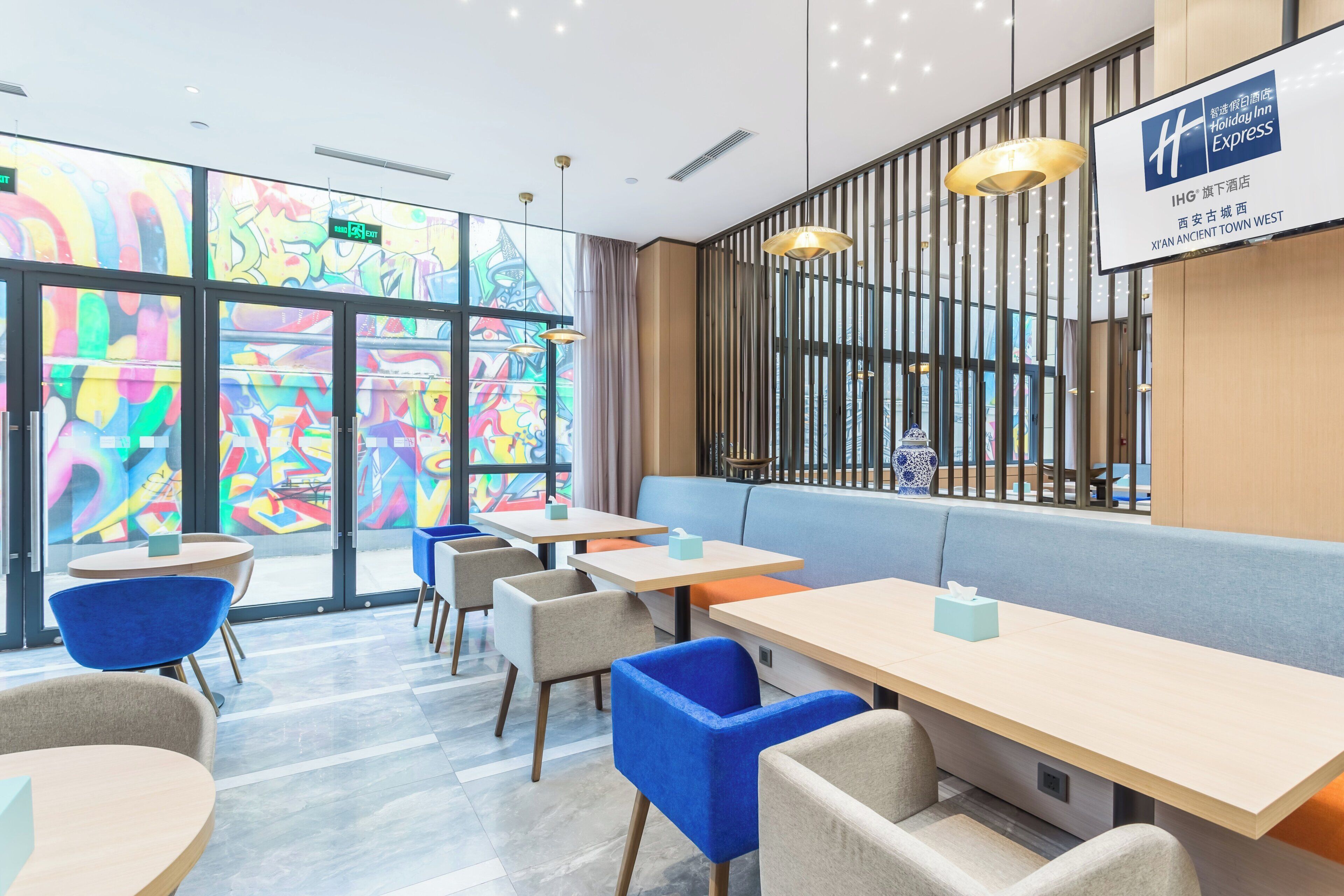 A modern hotel lobby with a seating area, tables, and a colorful mural on the wall.
