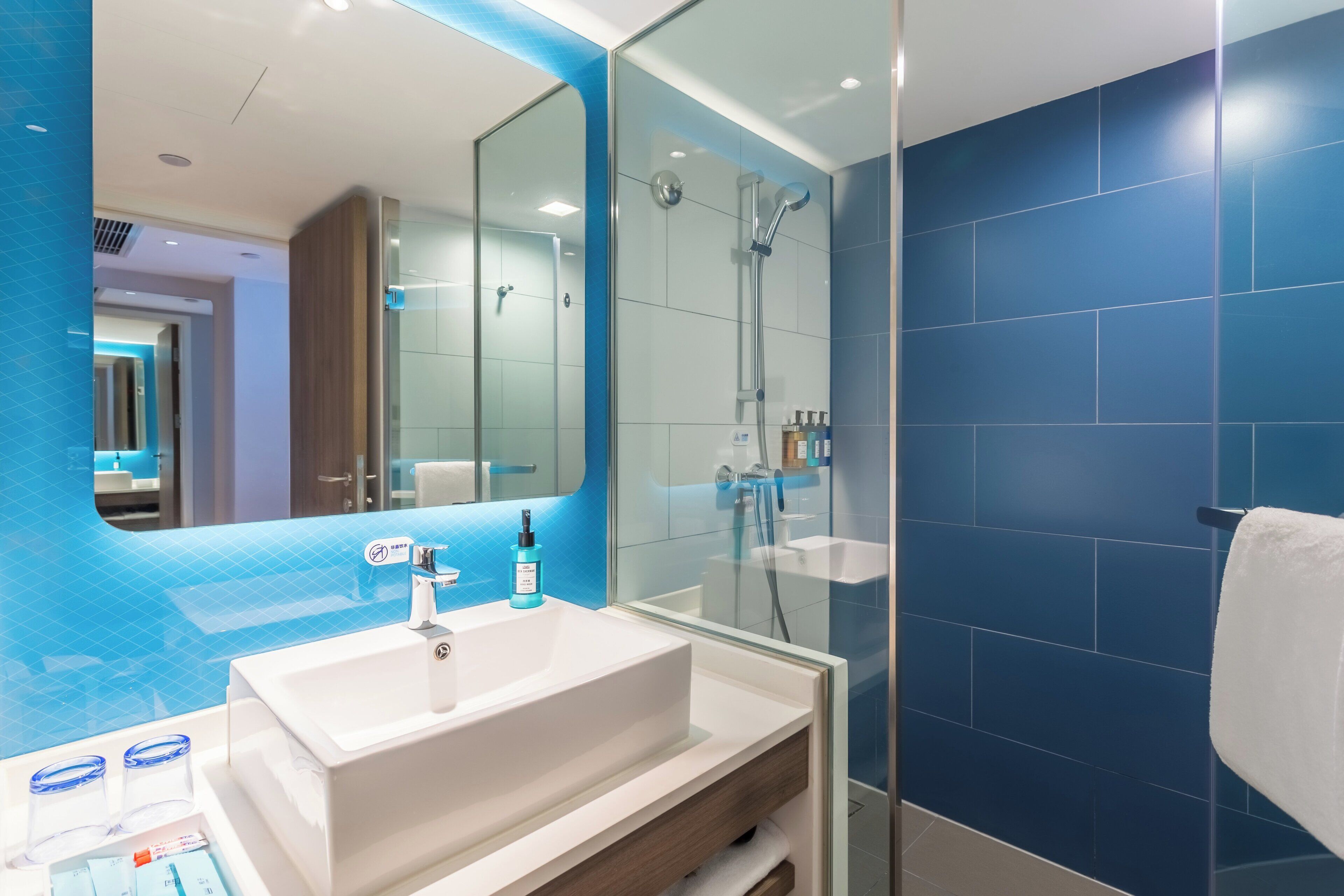 A modern bathroom with a large mirror, a white sink, and a glass-enclosed shower.