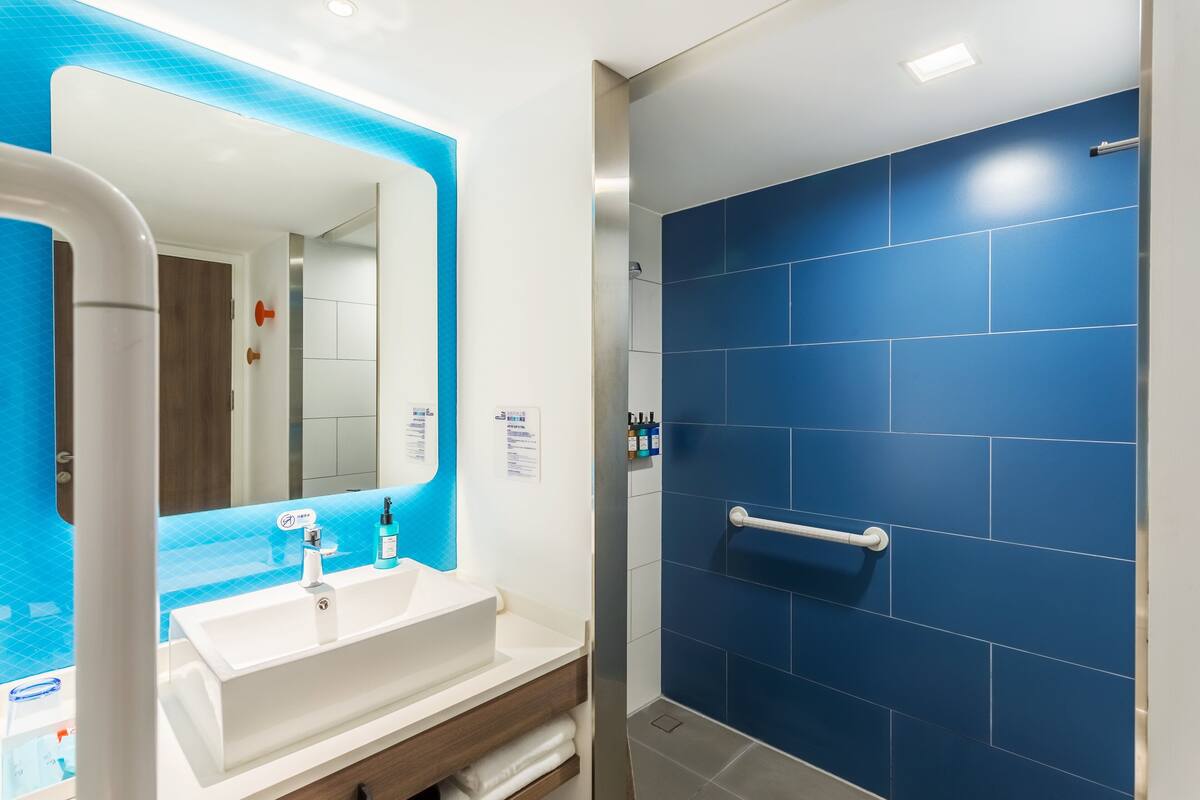 A bathroom with a white sink, blue-tiled shower, and a mirror with a blue frame.