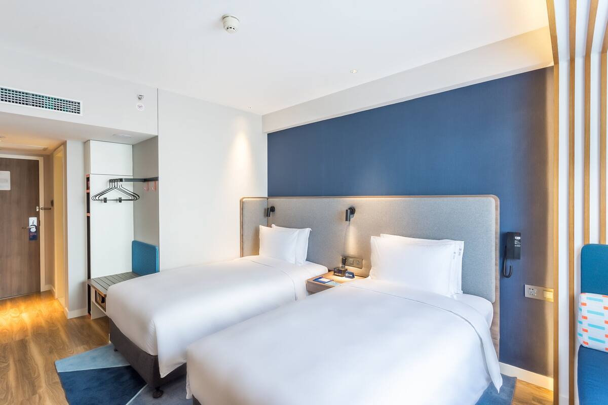 A hotel room with two beds, a desk, a chair, a wardrobe, and a bathroom.