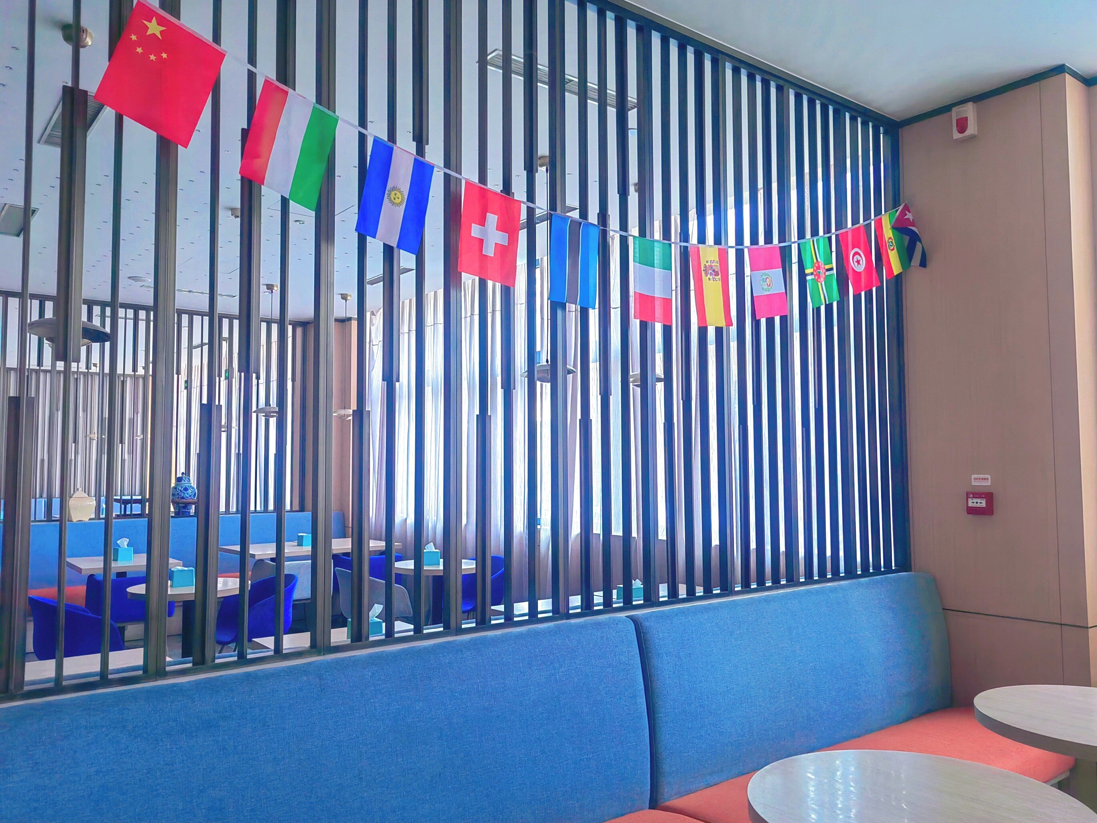 A seating area with a blue cushioned bench and a round table, separated by a metal partition with flags.
