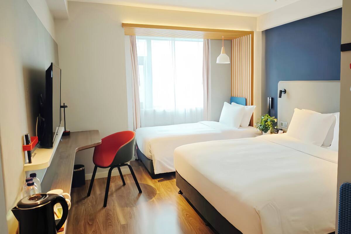 A hotel room with two beds, a desk with a chair, a television, and a window with curtains.
