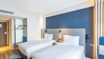 A hotel room with two beds, a wardrobe, a desk, and a bathroom.