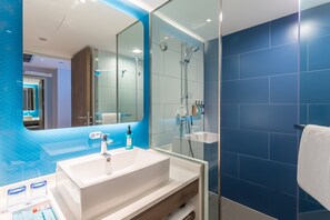 Ein modernes Badezimmer mit einem großen Spiegel, einem weißen Waschbecken und einer Duschkabine aus Glas.