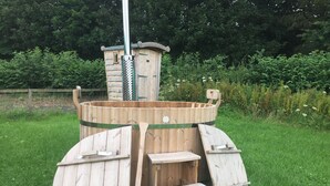 Ein hölzerner Whirlpool mit Stufen und Leiter, umgeben von viel Grün.
