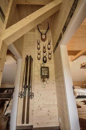 Een houten interieur met een schuine balken plafond, een hangklok en geweiherten.