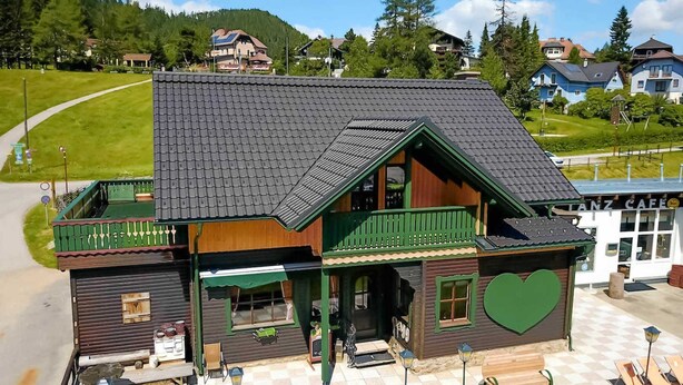 A wooden building with a green balcony, a checkered outdoor seating area, and a heart-shaped design on the side. - Steirer Apartment with Small Balcony - Steirer Apartment (Semmering-Kurort)
