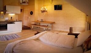 Um quarto aconchegante com cama, mesa de madeira, cozinha e lareira.