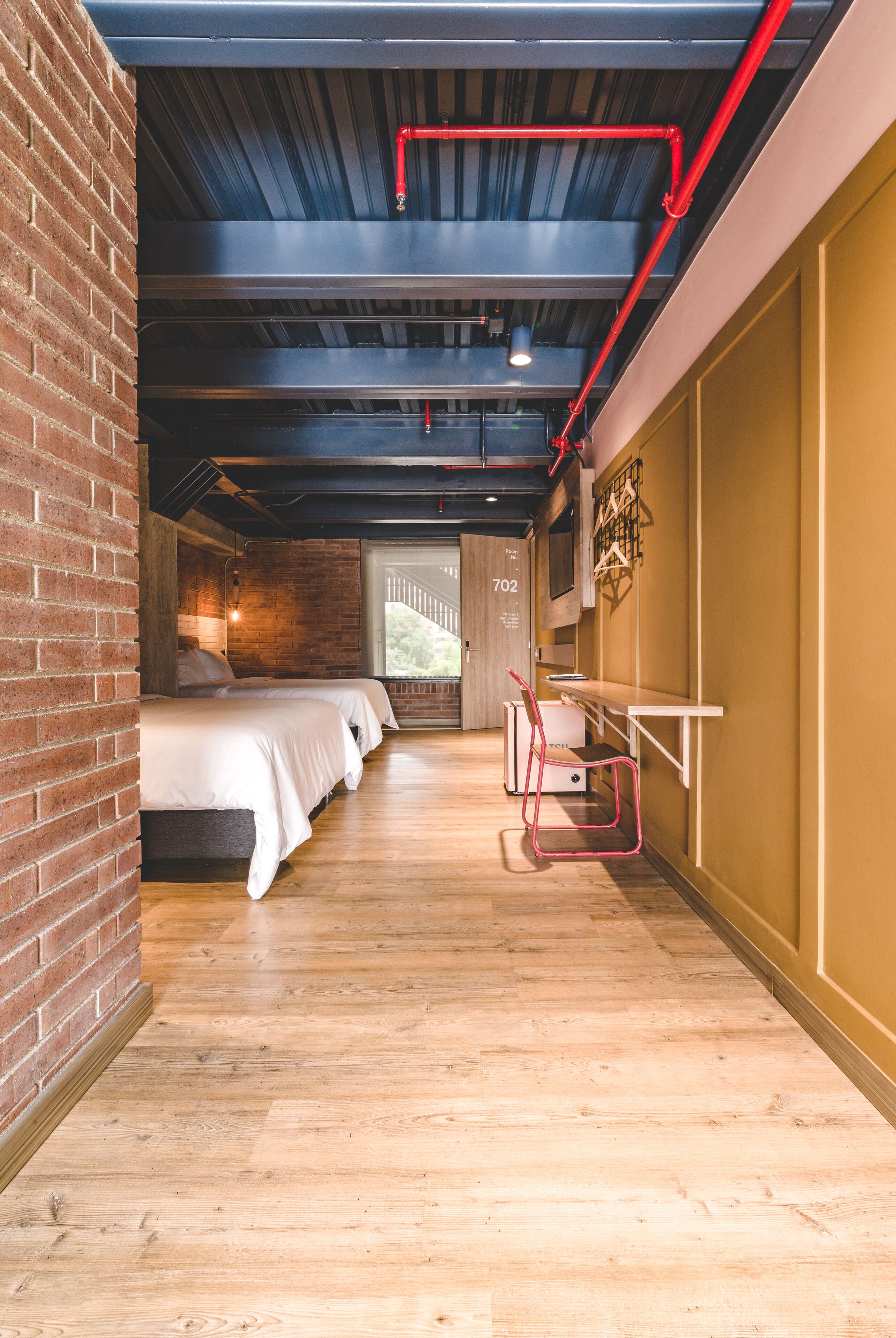 Une chambre d’hôtel avec un mur en briques, un plancher en bois, un lit, un bureau et une chaise.