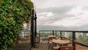 A wooden deck with tables and chairs, surrounded by greenery and overlooking a cityscape. - The Somos Beats Hotel  (Medellín)