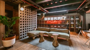 A modern lounge area with a sofa, two wooden stools, a potted plant, and a neon sign. - The Somos Beats Hotel  (Medellín)