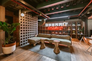 Un área de descanso moderna con un sofá, dos taburetes de madera, una planta en maceta y un letrero de neón.