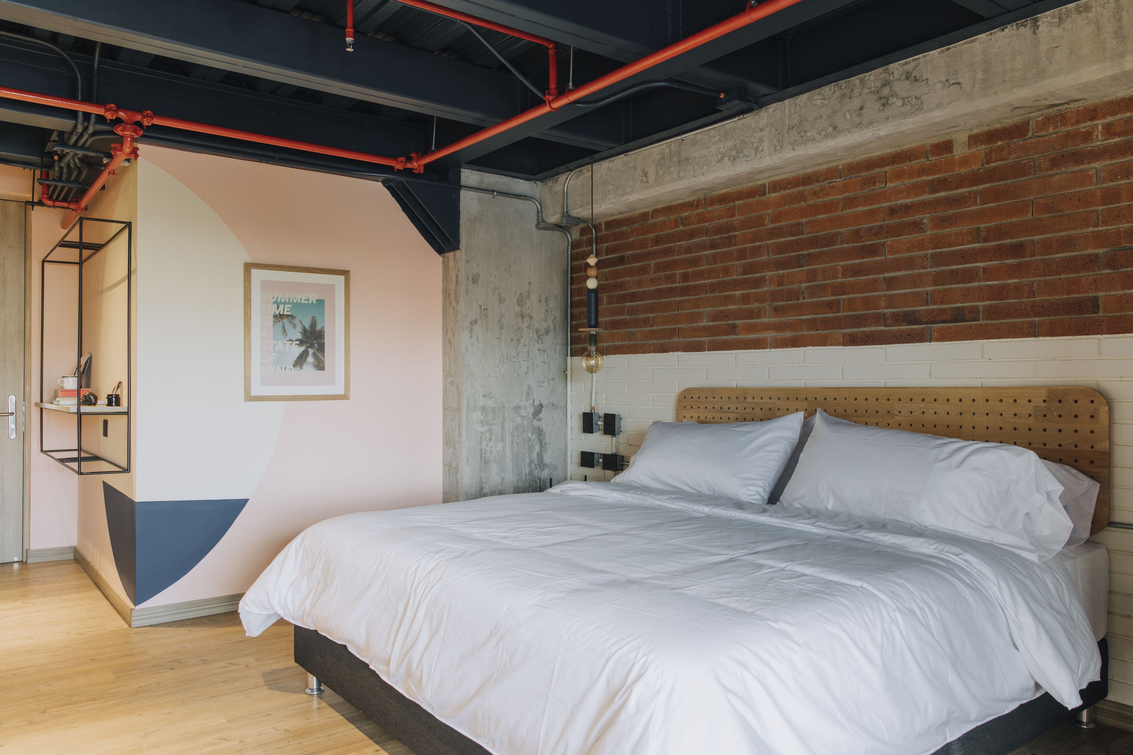 Un dormitorio moderno con pared de ladrillo, cabecera de madera y colcha blanca.