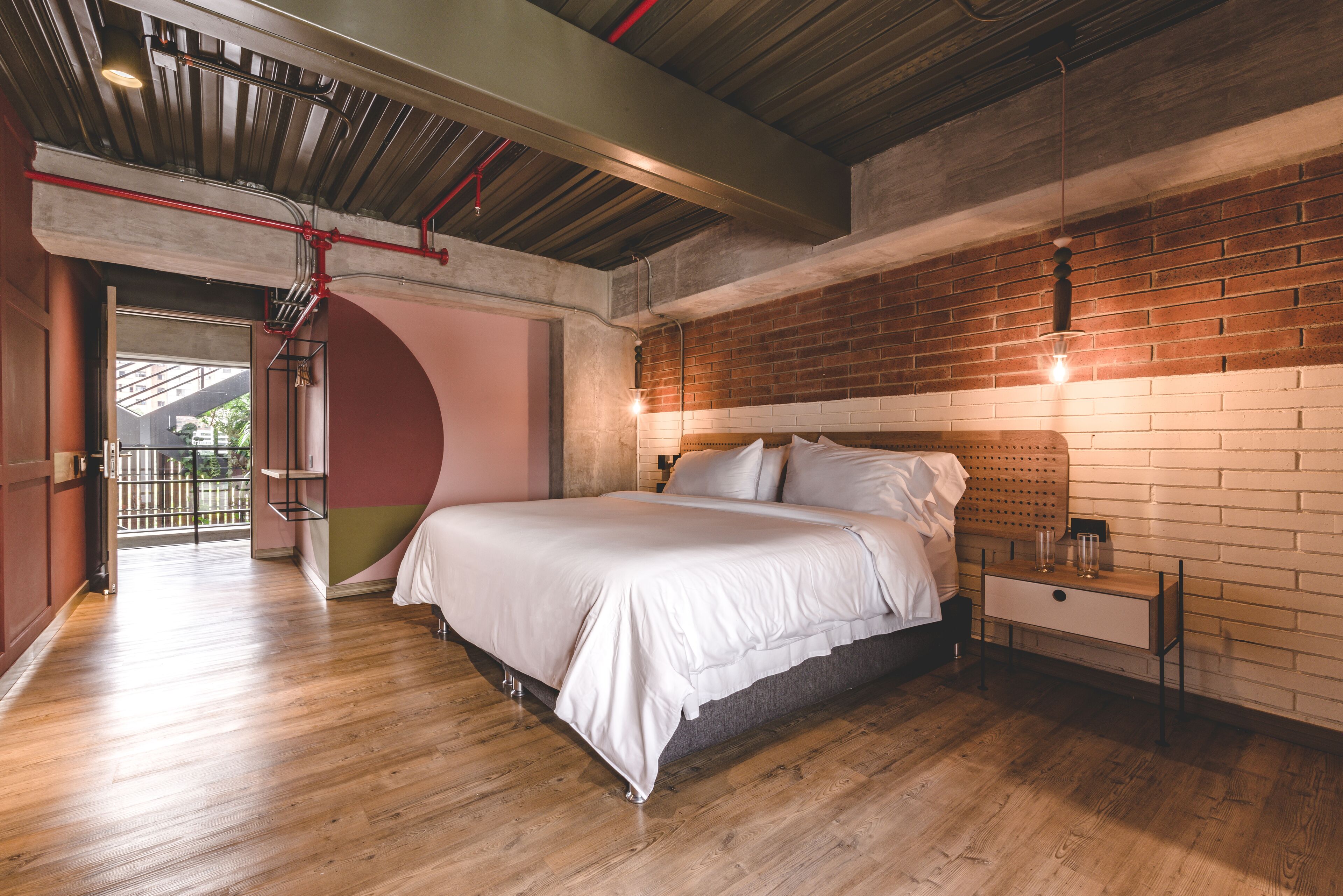 A modern bedroom with a large bed, wooden flooring, a brick wall, and a skylight.
