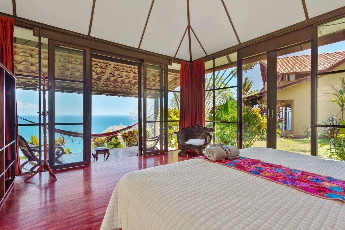 Een ruime slaapkamer met een groot bed, een stoel en een hangmat met uitzicht op een prachtig panorama.