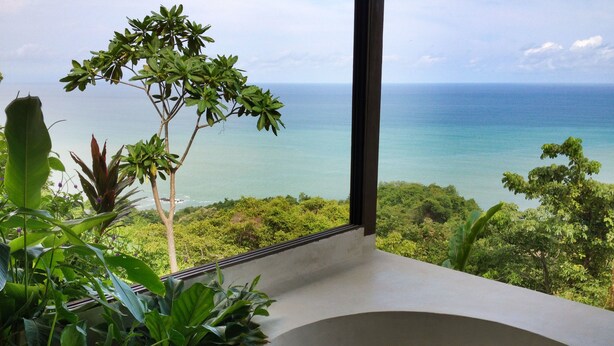 A room with a large window overlooking a tropical landscape and the ocean. - Anamaya (Cóbano)