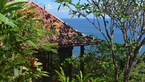 A rustic house with a tiled roof, surrounded by lush greenery and overlooking a body of water. - Anamaya (Cóbano)