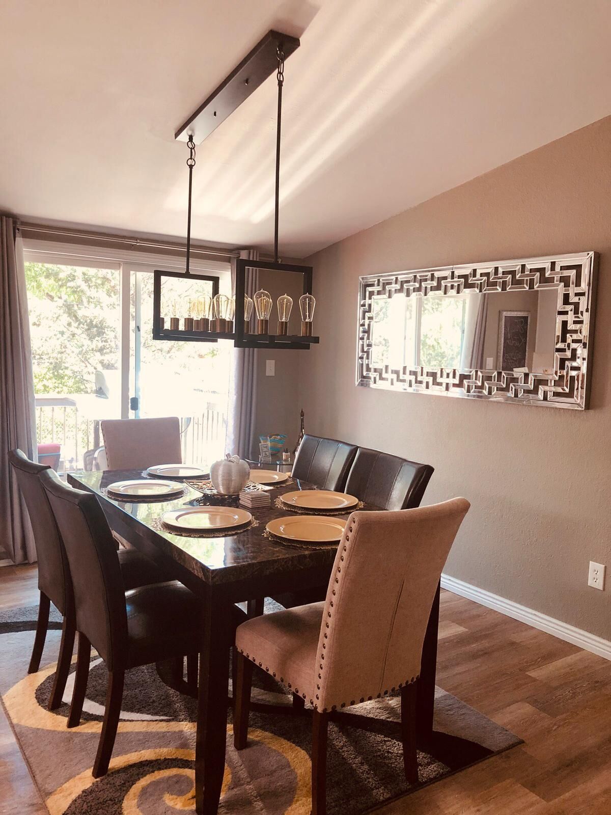 A dining area with a large table, chairs, a chandelier, and a decorative mirror.