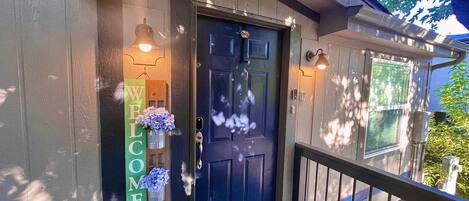 A wooden house with a dark blue front door, a welcome sign, and a porch with a railing.