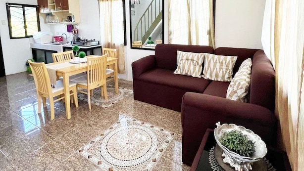 A living room with a sofa, a dining table with chairs, a kitchen area, and a staircase. - Town House Next to the Beach - TALOMO TORIL DAVAO (Talomo)