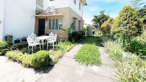 A two-story house with a patio area featuring a white table and chairs, surrounded by greenery and a small garden. - Town House Next to the Beach - TALOMO TORIL DAVAO (Talomo)