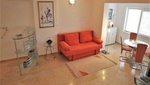 Un salon avec un canapé rouge, une table basse en verre, une étagère en verre et un coin repas comprenant une table et des chaises.