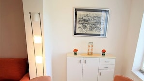 Un coin repas avec une table en verre, des chaises orange, un meuble blanc et une œuvre d’art encadrée au mur.