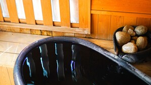 Una terraza de madera con un jacuzzi negro, una valla de madera y una cesta de piedras.