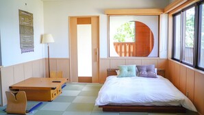 Habitación con cama, escritorio, silla, lámpara y ventana con vista a follaje.