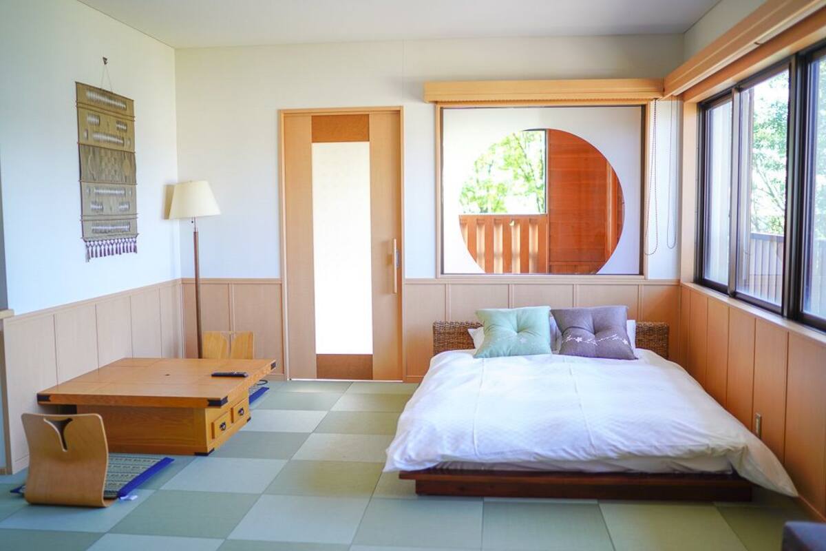 Ein Zimmer mit Bett, Schreibtisch, Stuhl, Lampe und einem Fenster mit Blick auf Grünflächen.