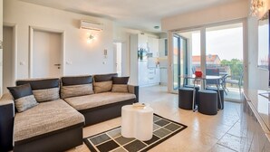 Un salon moderne avec un canapé d’angle, une petite table blanche et une table à manger en verre, accompagnée de chaises.