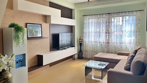 Una sala de estar moderna con un televisor de pantalla plana, una mesa de centro de vidrio, un sofá y una planta decorativa.