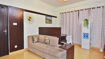 A modern living room with a sofa, a coffee table, a decorative wall piece, a framed picture, and a curtain with a hanging plant.