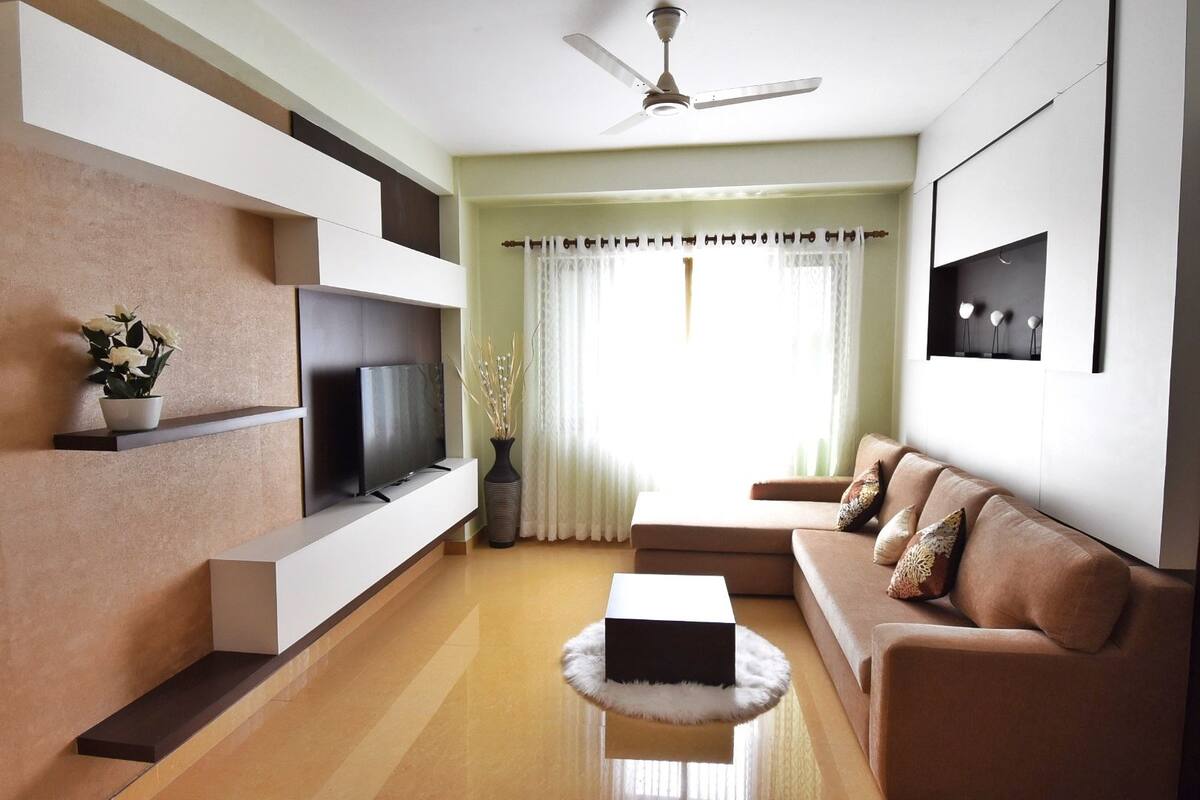 A modern living room with a flat-screen TV, a sofa, a coffee table, and a ceiling fan.