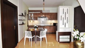 Una cocina compacta con armarios de madera, una isla central y una zona de comedor con sillas blancas.
